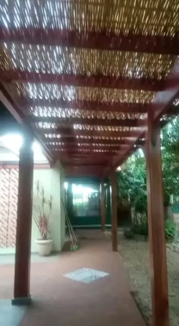 Pergolado de madeira com cobertura de bambu sobre um corredor externo